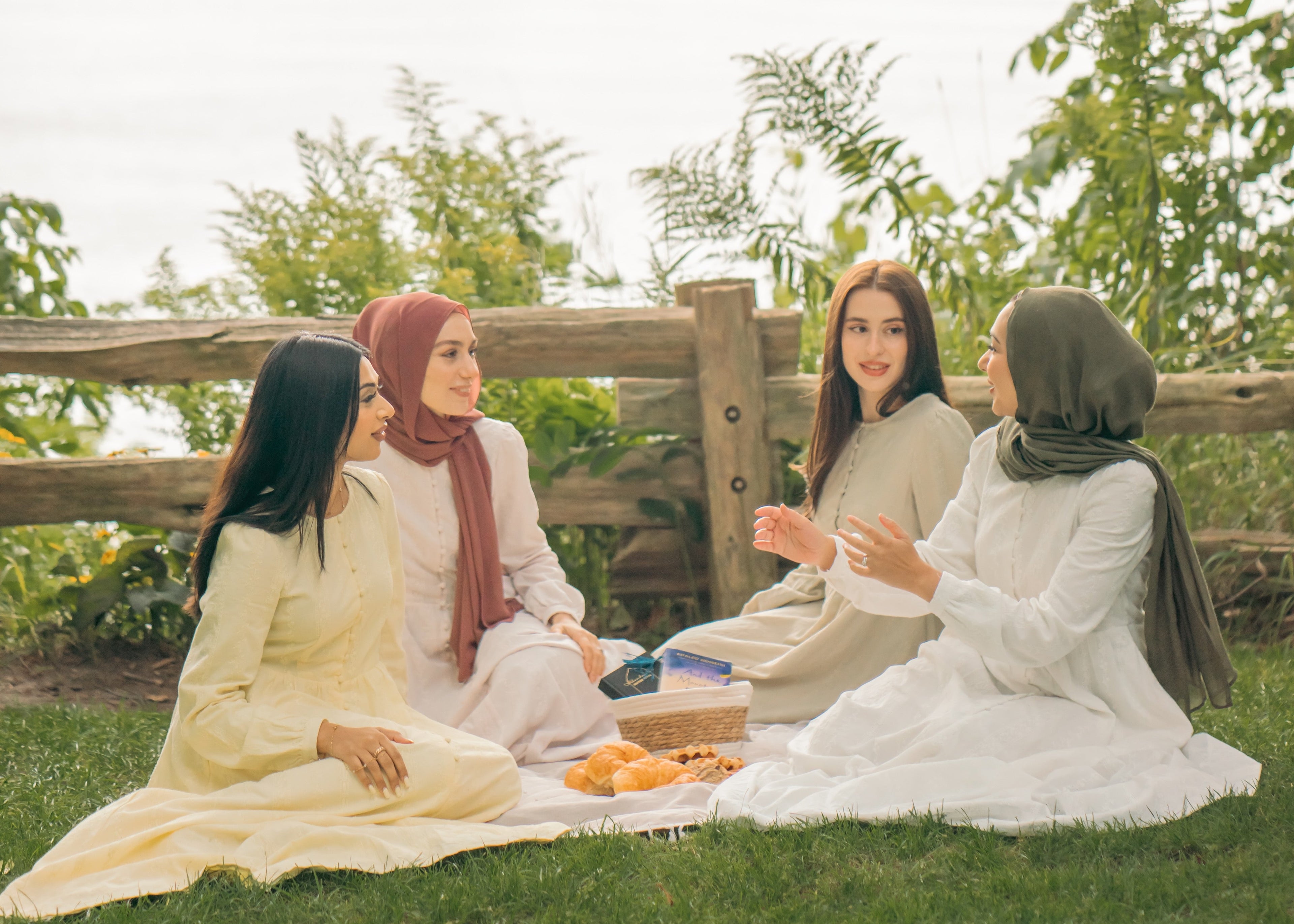 Four women sitting on a blanket in a park, enjoying a picnic.